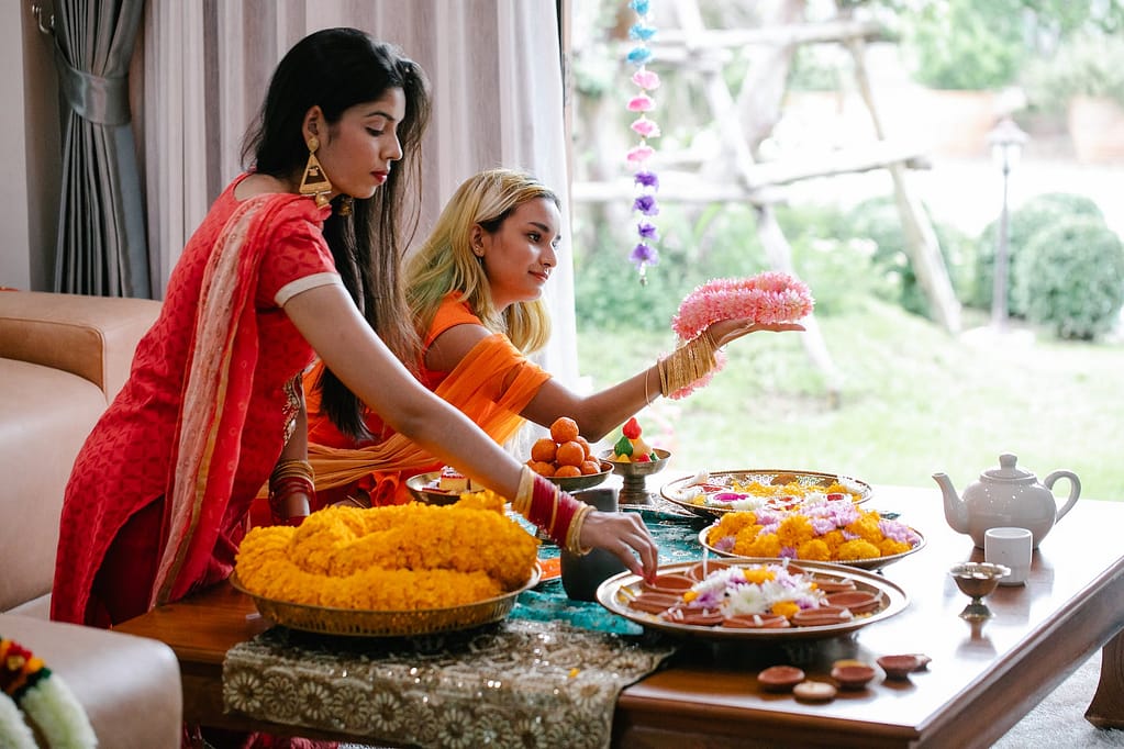 women wearing sari preparing flower necklaces and traditional snacks