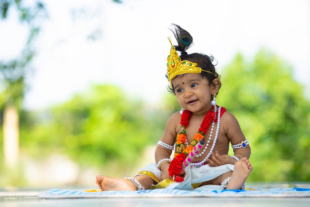 cheerful little ethnic child in traditional accessories sitting in garden